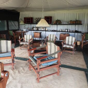 stoelen en tafels van hout in een lodge met op de achtergrond een bar en vloerkleden op de grond